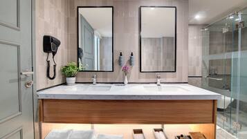 A modern bathroom with two sinks, a hairdryer, a potted plant, and a shower area.