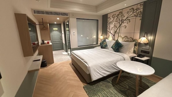 A modern hotel room with a bed, bedside table, lamp, and a view of the hallway.