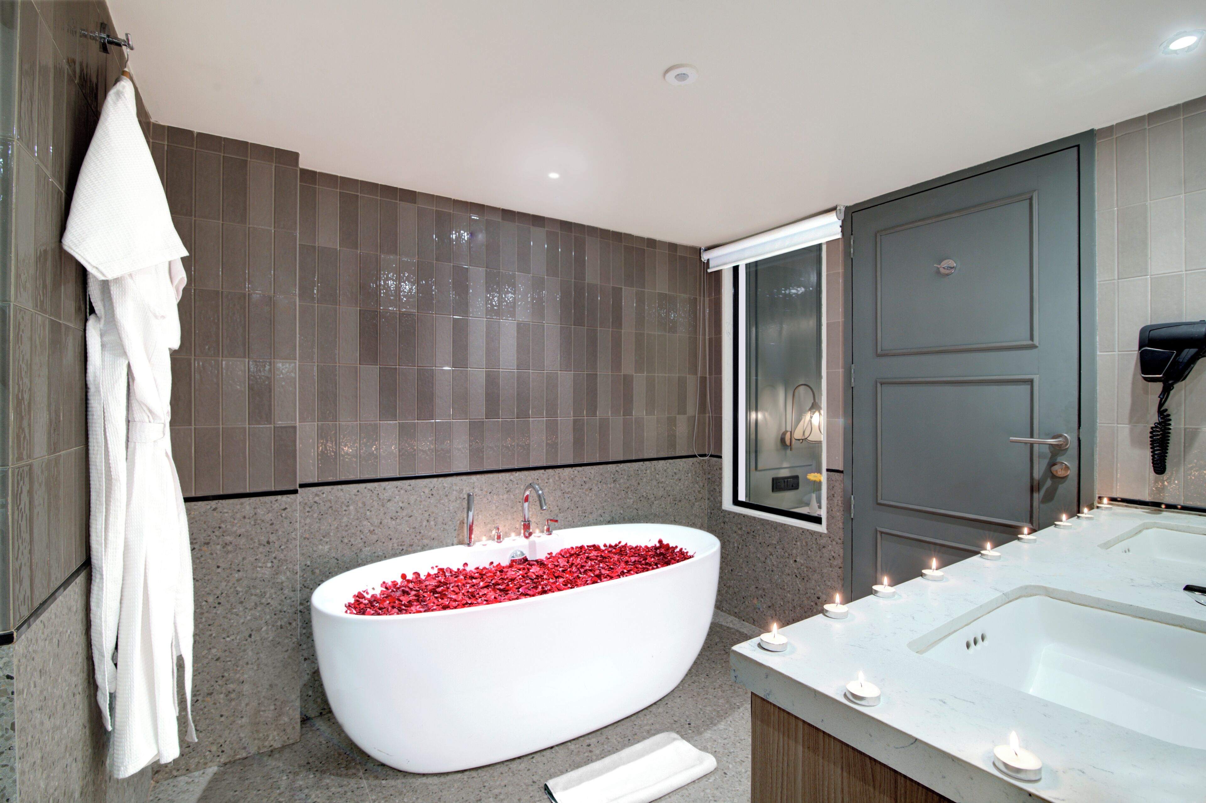 A modern bathroom with a freestanding bathtub filled with red pebbles, a separate shower area, and a vanity with a mirror.