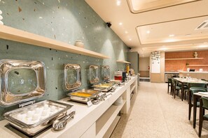 Zona de bufé con varios dispensadores de alimentos y un área de comedor con mesas y sillas.