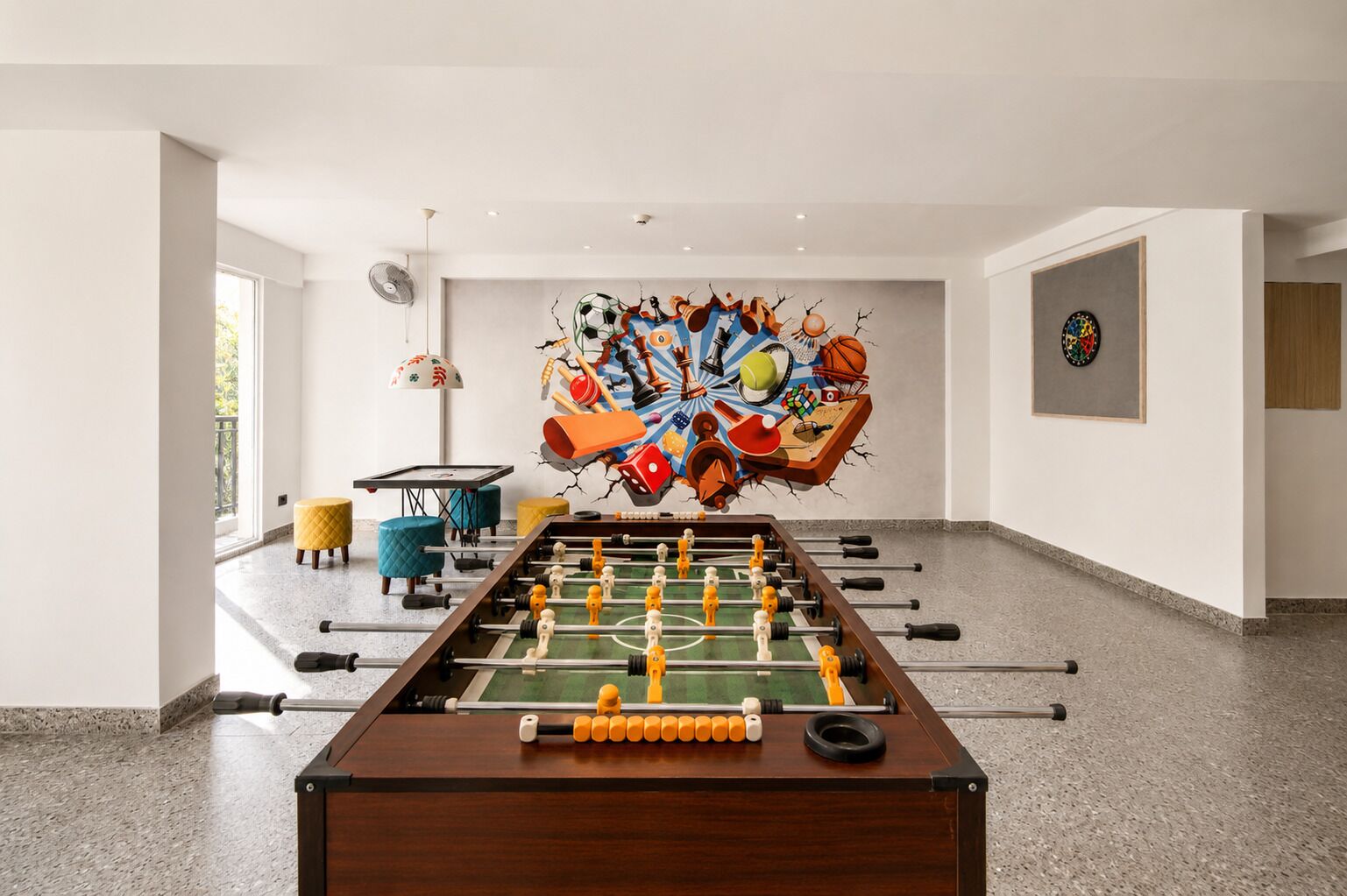 Een kamer met een tafelvoetbaltafel, een dartbord en een kunstwerk aan de muur.