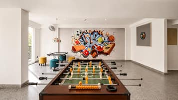 Een kamer met een tafelvoetbaltafel, een dartbord en een kunstwerk aan de muur.
