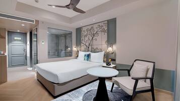 Habitación de hotel moderna con cama, una silla, una mesita y ventilador de techo, además de ducha.