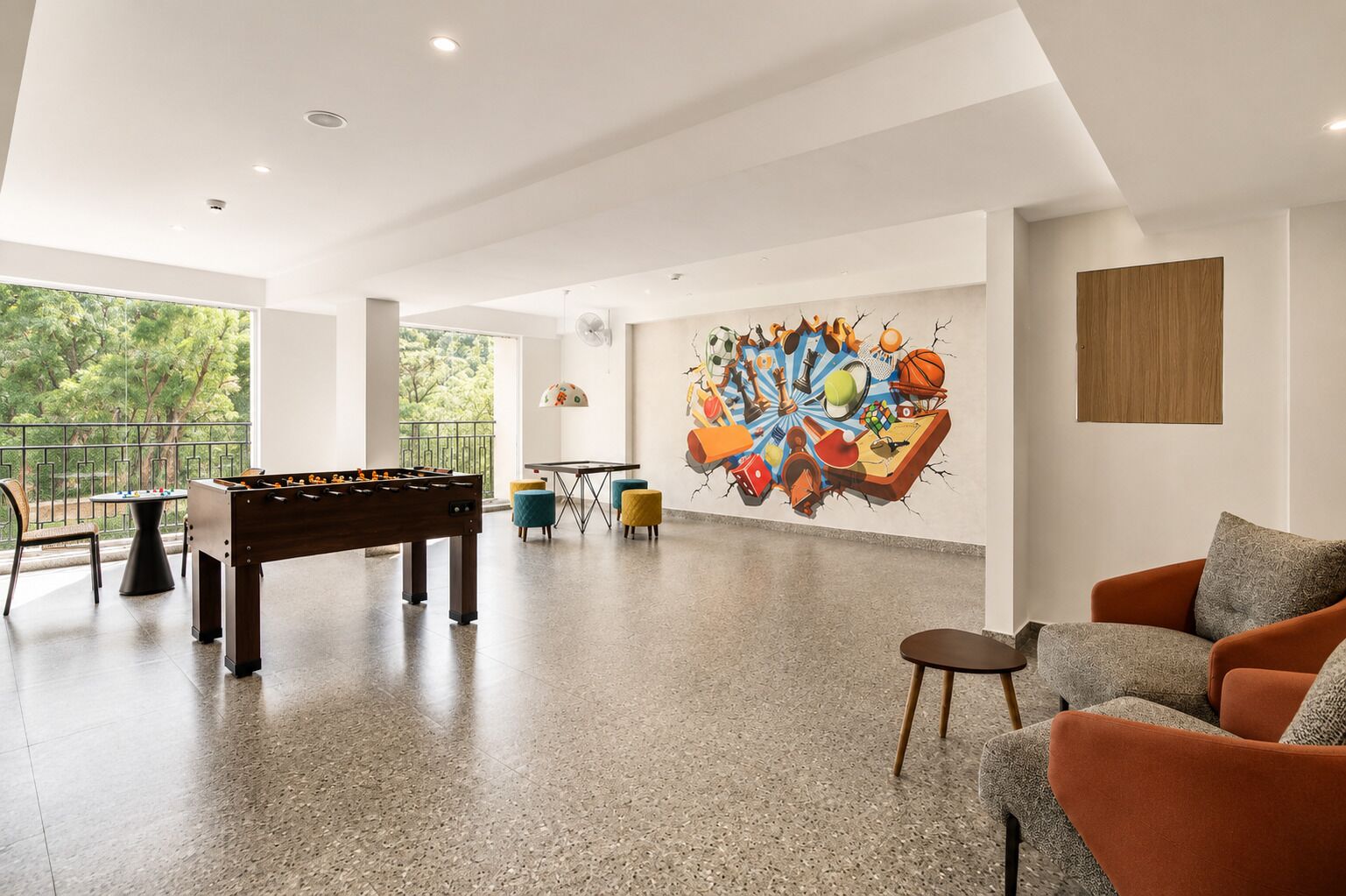 Una habitación amplia con mesa de fútbol de mesa, mesa de ping pong y un mural colorido en la pared.