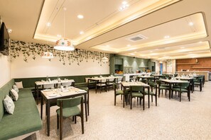 Un restaurante amplio con varias mesas y sillas, un sofá verde y una zona de cocina.