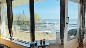 Una habitación con un ventanal grande con vista a un puerto deportivo, una mesita redonda con una vela y un sofá gris.