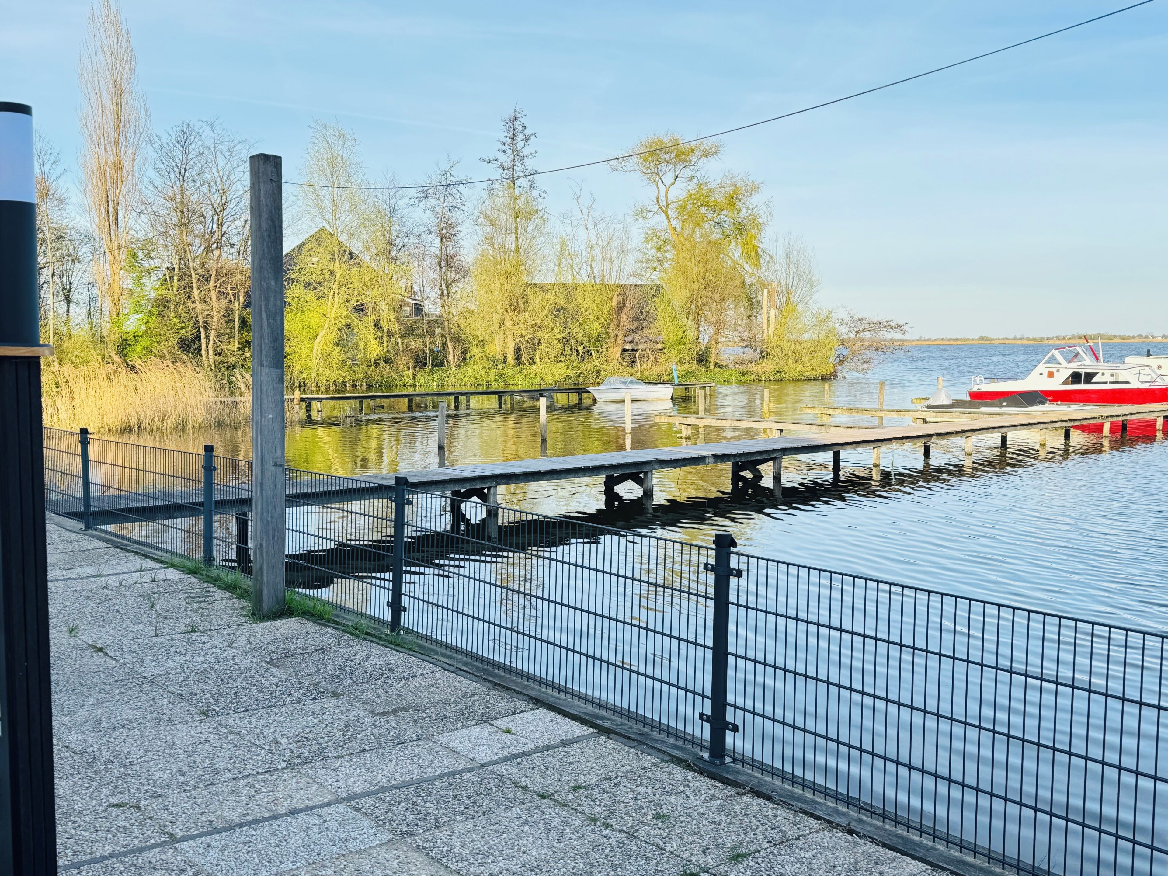 Ein Uferbereich mit Anlegesteg, einem Boot und einem Fußweg.