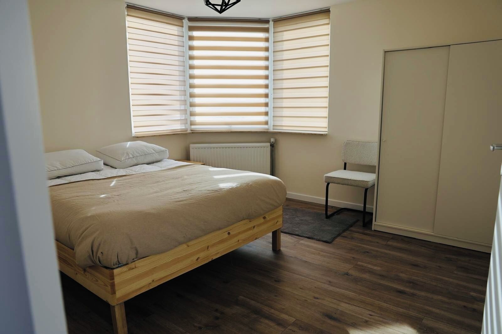 A bedroom with a wooden bed, a radiator, a chair, and a wardrobe.