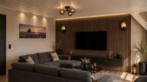 Una sala de estar moderna con un sofá modular, un televisor de pantalla plana y un estante de pared con objetos decorativos.
