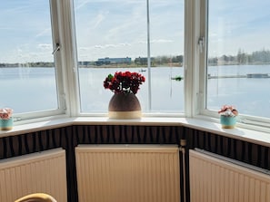 Une pièce dotée d’une baie vitrée donnant sur un plan d’eau, d’un radiateur et d’un coin avec une petite table.