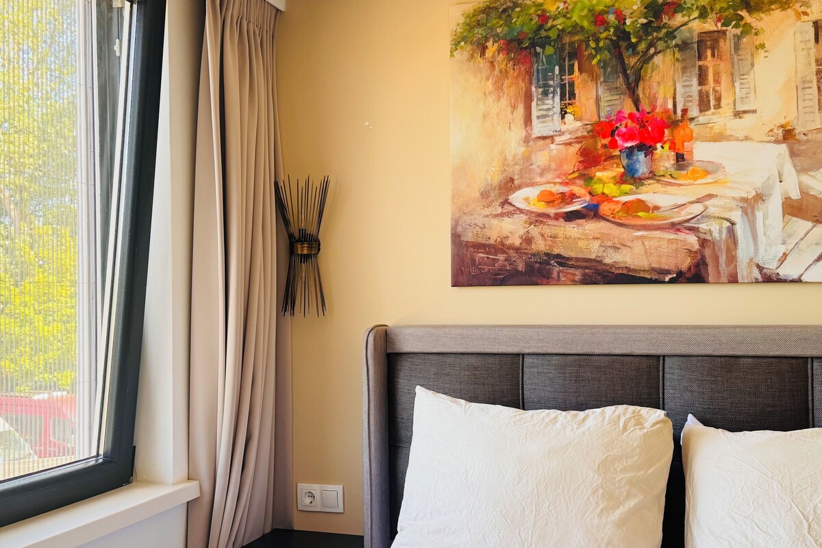 Quarto com cama, janela com cortinas, quadro na parede e tomada.