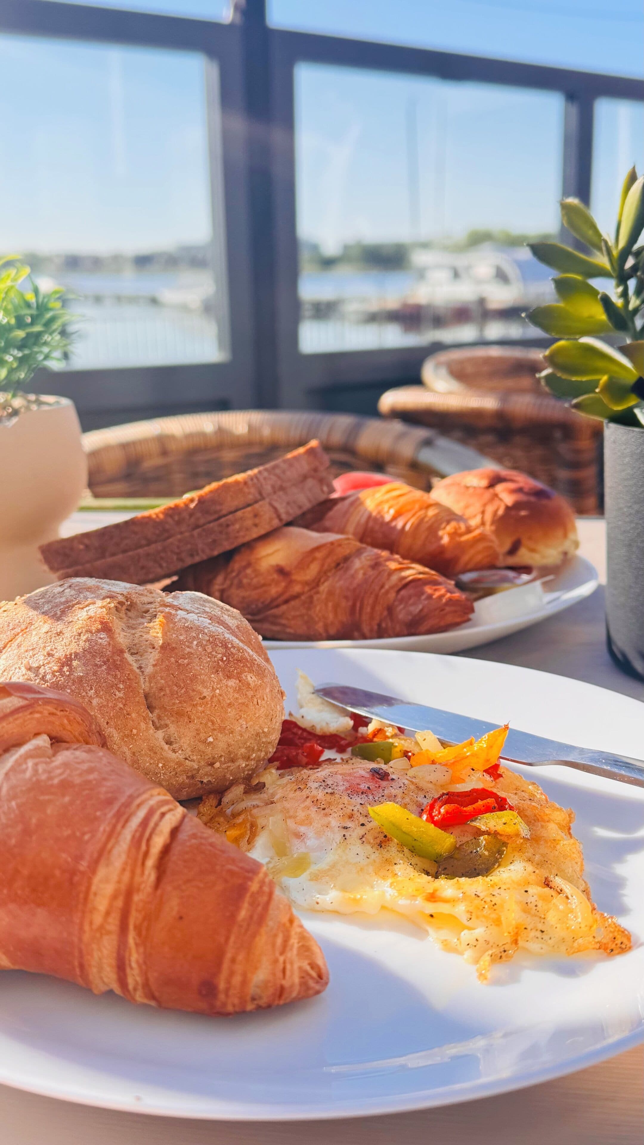 Un desayuno con cruasanes, pan y un plato de huevos con verduras.