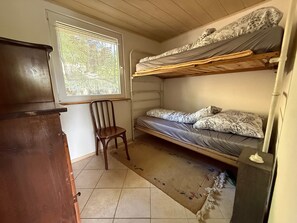 A small room with a bunk bed, a wooden chair, and a window.