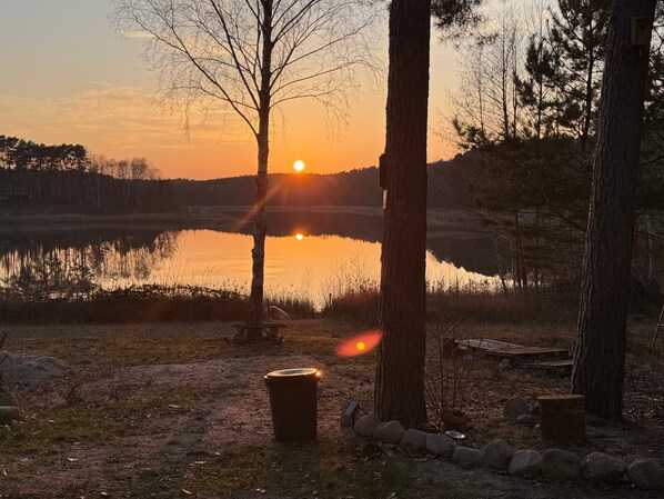 A sunset over a calm lake with trees and a bench.