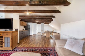 A spacious living area with exposed wooden beams, a television, a dining table with chairs, and a patterned rug.