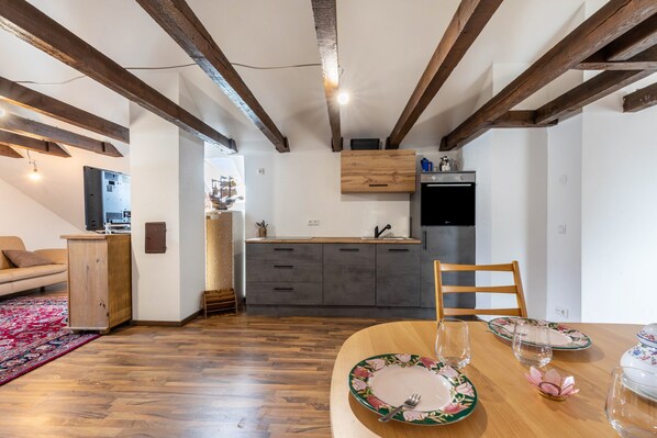 A modern kitchen with wooden beams, a dining table set with plates and glasses, and a sofa in the adjacent living area.