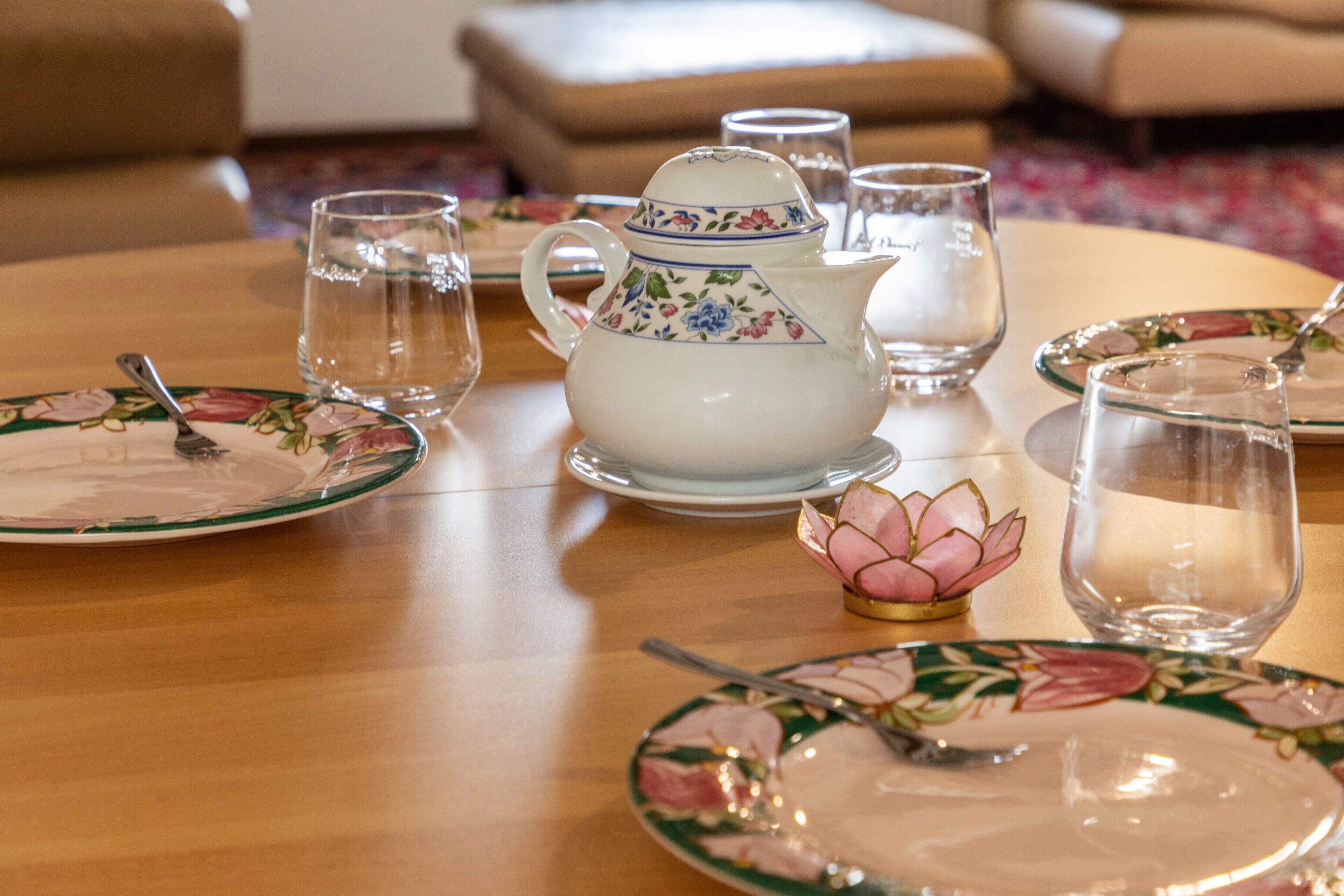 A dining table set with floral-patterned plates, a pitcher, and glasses.