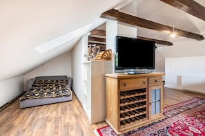 Un dormitorio tipo loft con techo inclinado, una cama, un televisor, un armario de madera con espacio para vinos y una alfombra estampada.