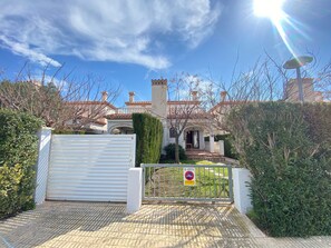 A gated entrance to a building with a tiled roof, a white garage door, and a sign indicating no parking. - Vila Magraners - Miami Playa (Mont-roig del Camp)