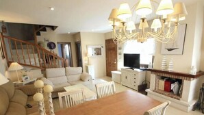 Una sala de estar con una escalera de madera, un comedor con una mesa de madera y una chimenea.