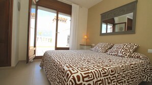 Un dormitorio con cama, espejo, ventana con cortinas y vistas al exterior.