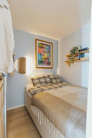 A bedroom with a bed, a bedside table, a lamp, a framed poster on the wall, and a bookshelf with books. - Panoramic views and sunsets atop Grünerløkka (Oslo)