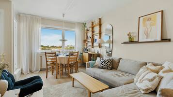 En moderne stue med sofa, sofabord, spisebord med stole og bogreol.