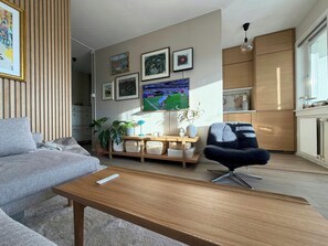 Ein modernes Wohnzimmer mit Sofa, Couchtisch, Fernseher, gerahmten Bildern und einer Küchenzeile.