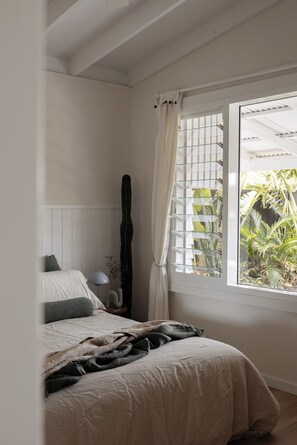 A bedroom with a bed, a window with curtains, a guitar, and a plant visible through the window. - Relaxed Coastal Retreat in Falcon – Perfect for Families (Falcon)