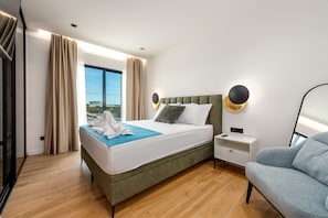 Ein modernes Hotelzimmer mit einem großen Bett, einem Nachttisch, einer Sitzecke und Blick durch das Fenster.