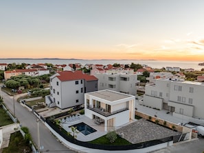 Ein Wohngebiet mit modernen Gebäuden, einem Schwimmbad und Blick auf das Meer bei Sonnenuntergang.