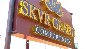 A sign for SKVR GRAND with a lotus flower logo and the words 'COMFORT STAY'. - Hotel SKVR Grand - Theni  (Periyakulam)