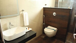 A bathroom with a white sink, a mirror, a towel, a shower, and a toilet. - Hotel SKVR Grand - Theni  (Periyakulam)