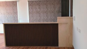 A reception desk with a wooden panel, a beige counter, and a textured wall. - Hotel SKVR Grand - Theni  (Periyakulam)