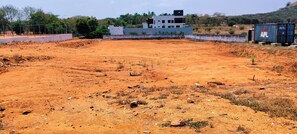 A construction site with a large open area, a building in the background, and shipping containers on the right. - Hotel SKVR Grand - Theni  (Periyakulam)
