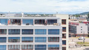 Un edifici de diverses plantes amb balcons, grans finestres i una vista de muntanyes al fons.