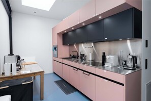 Eine moderne Küche mit rosa Schränken, einer Edelstahl-Arbeitsplatte und einem Oberlicht.
