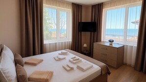 Quarto de hotel com cama, escrivaninha, televisão e vista para o mar.