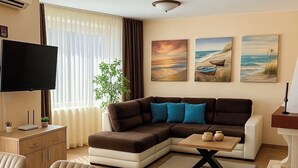 Uma sala de estar com sofá seccional, televisão de tela plana, mesa de jantar e uma planta.