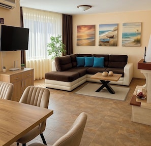 A living room with a sectional sofa, a flat-screen TV, a dining table, and a plant.