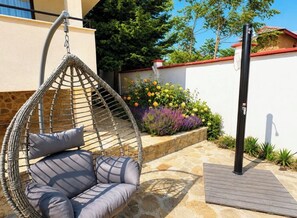 A hanging chair with cushions, a stone patio, and a garden with flowers and plants.