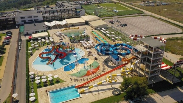 Um parque aquático com várias piscinas e toboáguas, cercado por estacionamento e edifícios.