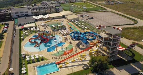 Parque acuático con múltiples toboganes y piscinas, rodeado de un estacionamiento y edificios.