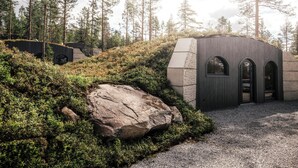 En modern byggnad med en fasad av sten, en välvd entré och en grusgång som leder fram till den.