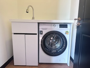 A compact washing machine and dryer unit with a sink, located in a room with a wooden floor and a dark door. - Lune&Palm Pool Villa (Pattaya City)