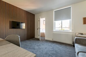 Ein modernes Zimmer mit einem an einer Holzvertäfelung befestigten Flachbildfernseher, einem großen Fenster mit Aussicht, einem grauen Teppich und einem grauen Sofa.