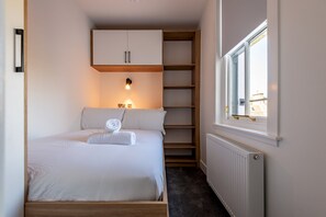 A bedroom with a bed, a wardrobe, a radiator, and a window with a view. - Marine Place | Flat 8 (St Andrews)