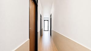A narrow, well-lit hallway with a wooden floor and white walls, leading to a door at the end. - FabHotel Metro Residency (Indore)