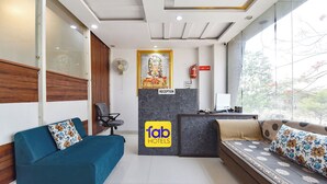 A hotel reception area with a reception desk, a blue sofa, a brown sofa, and a wall-mounted fan. - FabHotel Metro Residency (Indore)