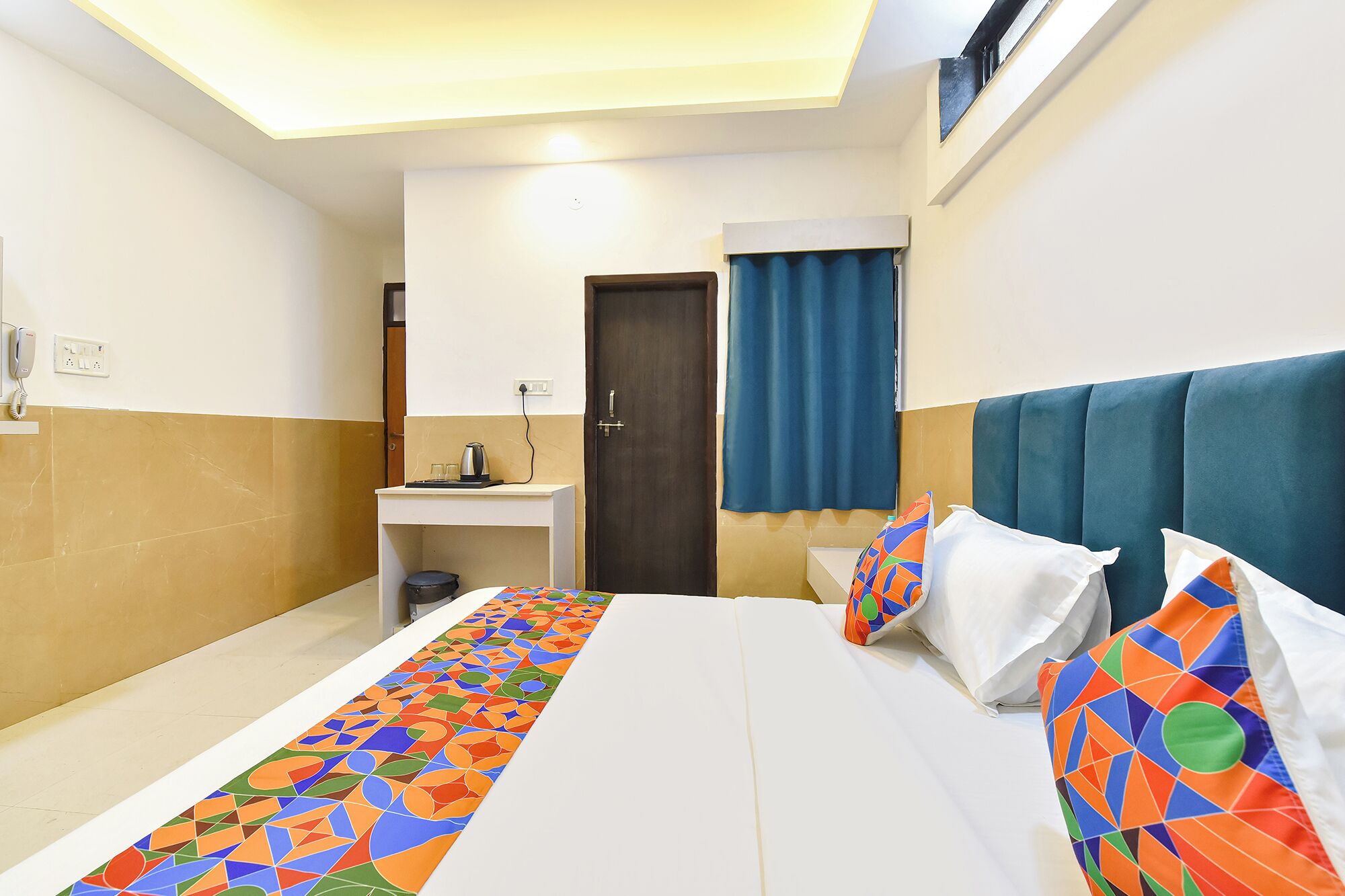 Een hotelkamer met een bed, nachtkastje en een klein bureau met telefoon en stopcontact.